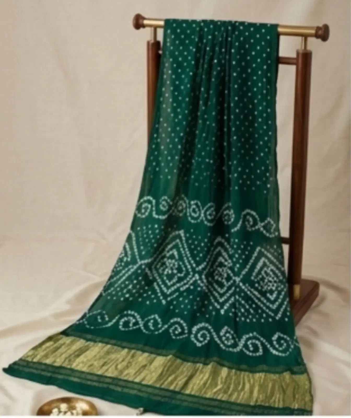 Green saree with white dotted bandhani-style patterns and a golden border draped on a wooden stand