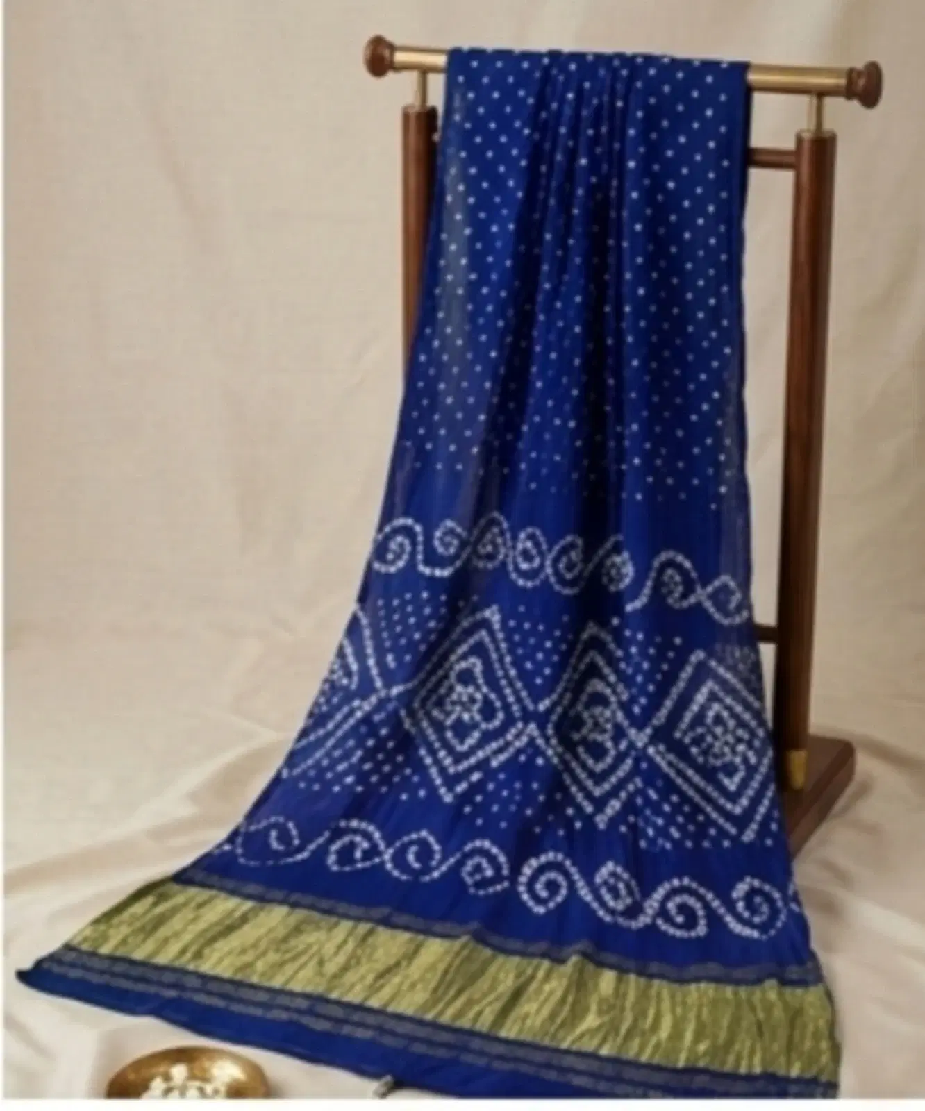 Blue saree with white dotted and geometric motifs and green border draped on a wooden stand