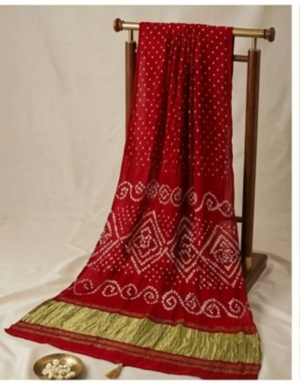 Red Bandhani-style saree with white dotted motifs and green border draped on a wooden stand