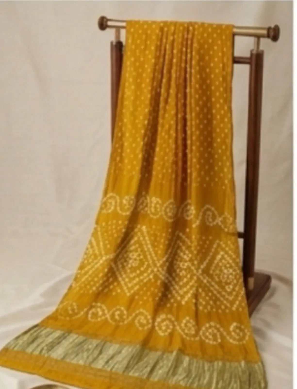 Mustard yellow printed saree with white dotted motifs and contrasting border draped on a wooden stand