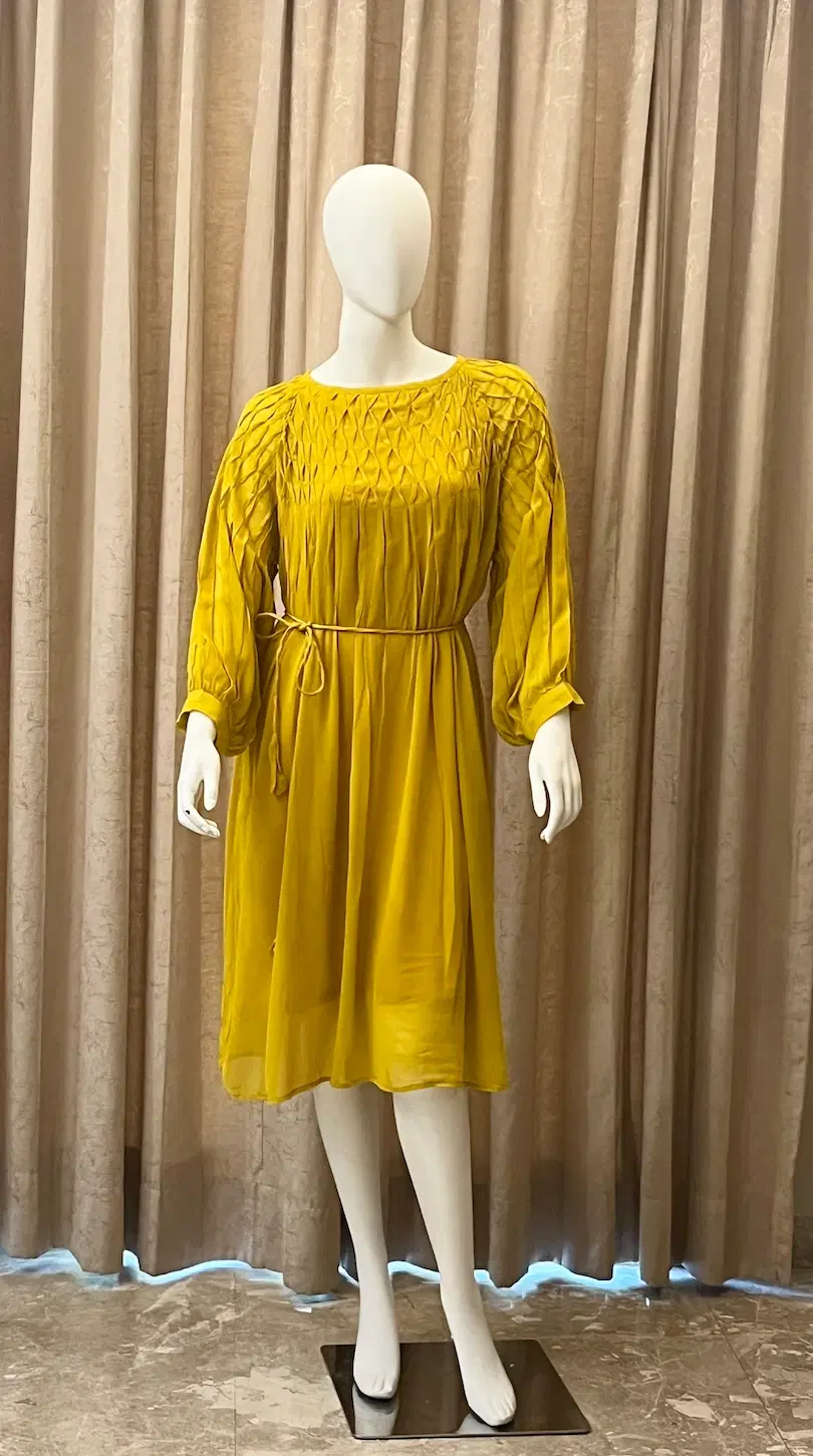 Mustard yellow knee-length women's dress with pleated bodice, long sleeves and tie waist on a mannequin