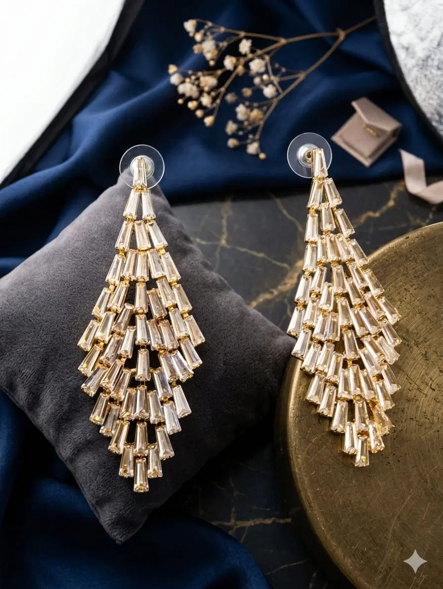 Pair of gold-tone cascading baguette crystal drop earrings displayed on a gray cushion