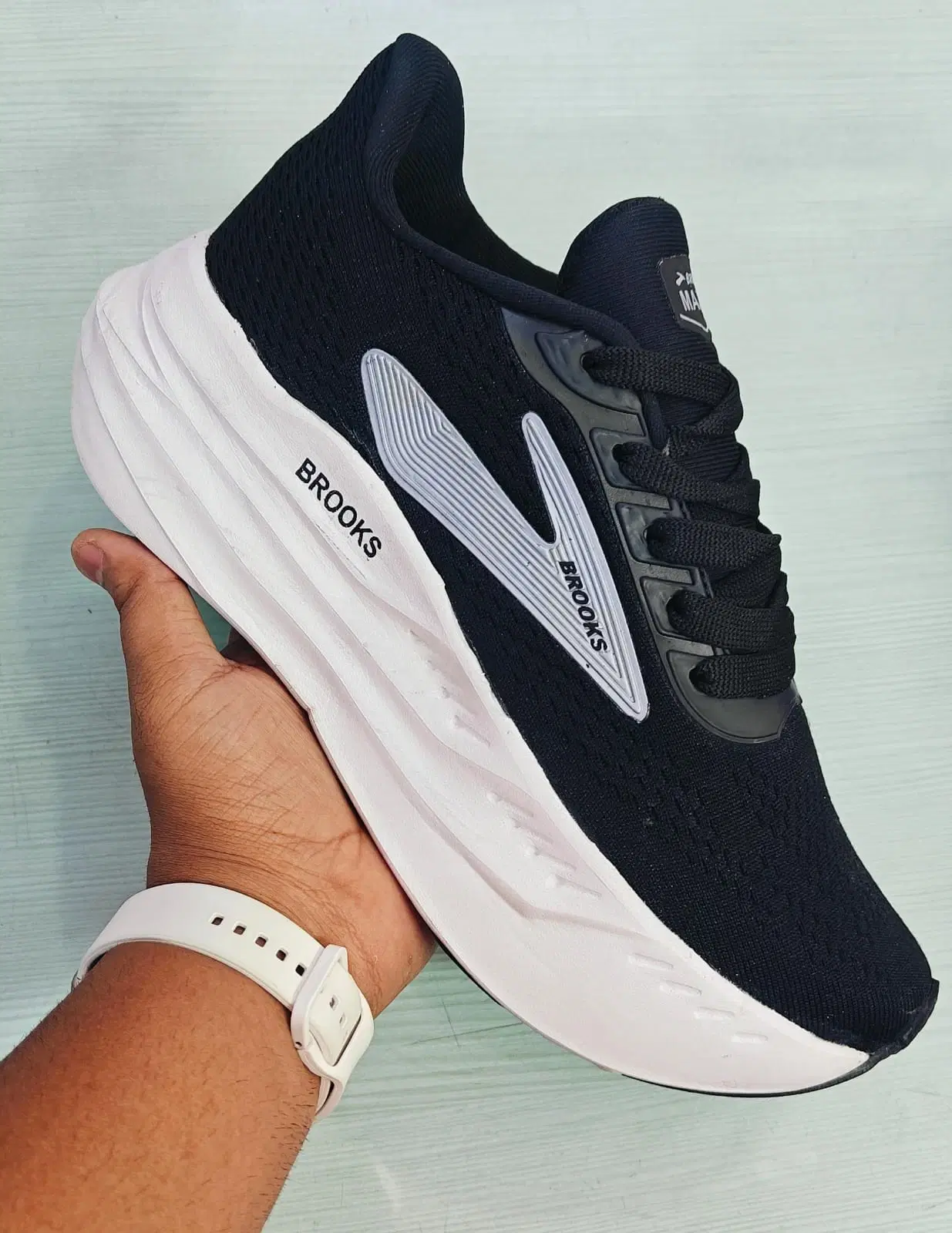 Black lace-up athletic shoe with thick white cushioned sole and Brooks branding held in hand