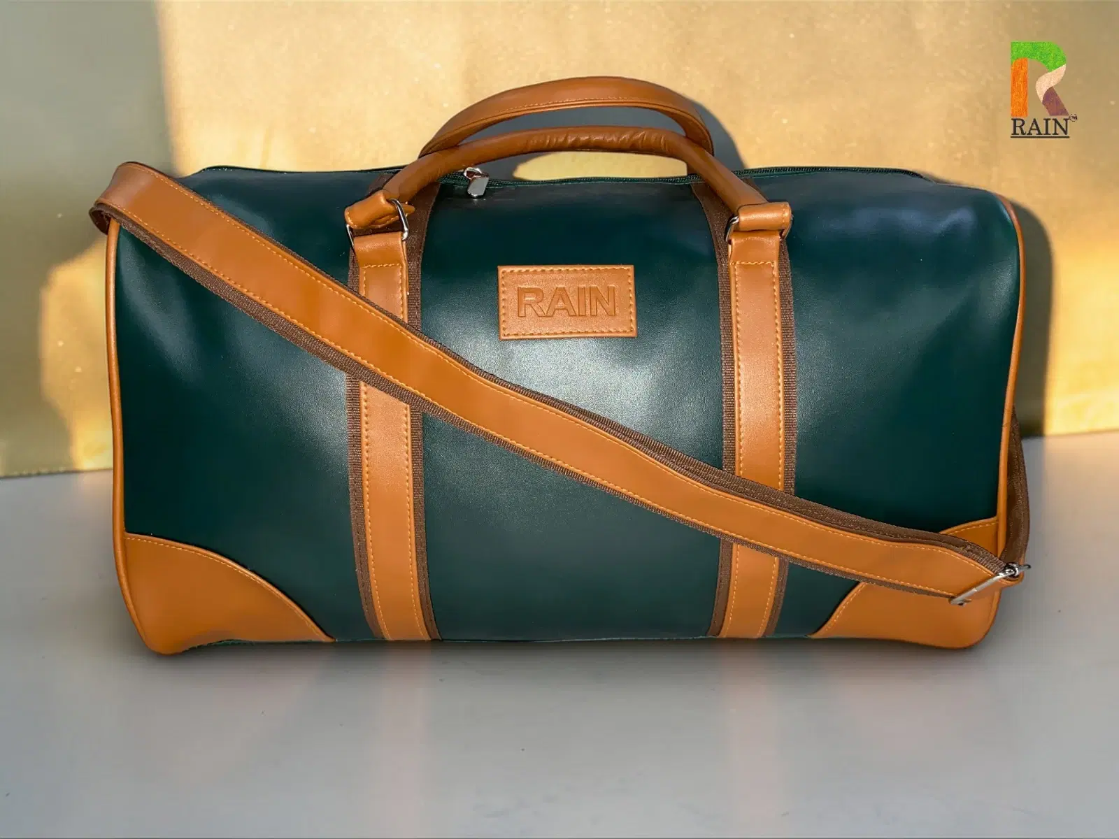 Green and tan duffel travel bag with top handles, shoulder strap, zip closure, and Rain logo