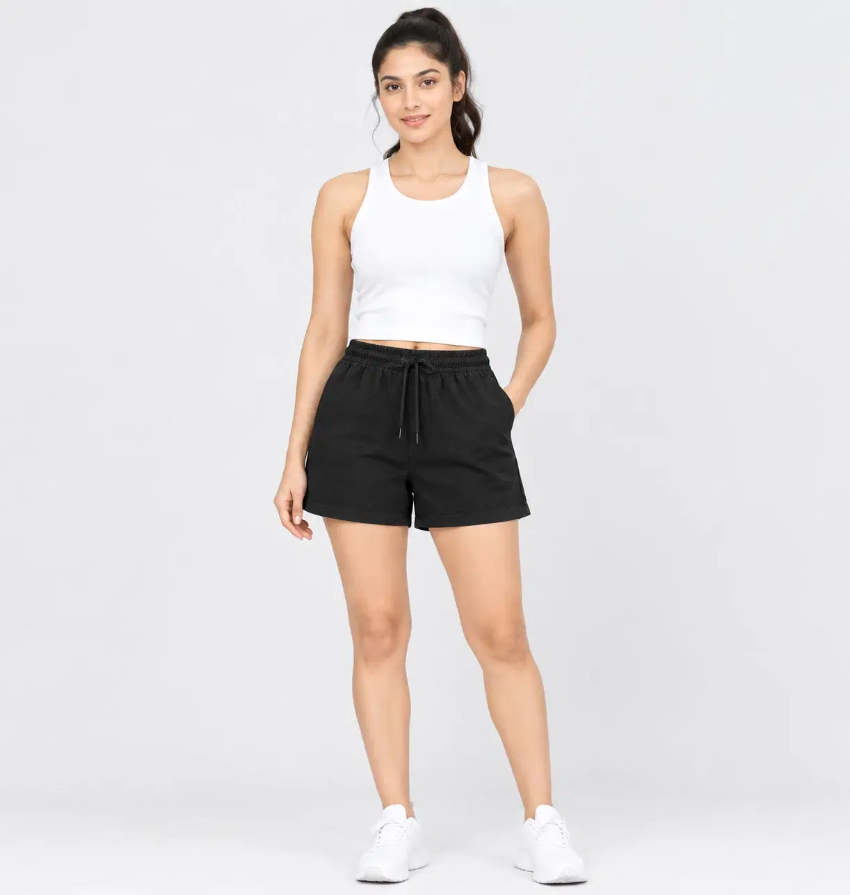 Front full-length view of black drawstring shorts with side pockets, styled with a white crop tank