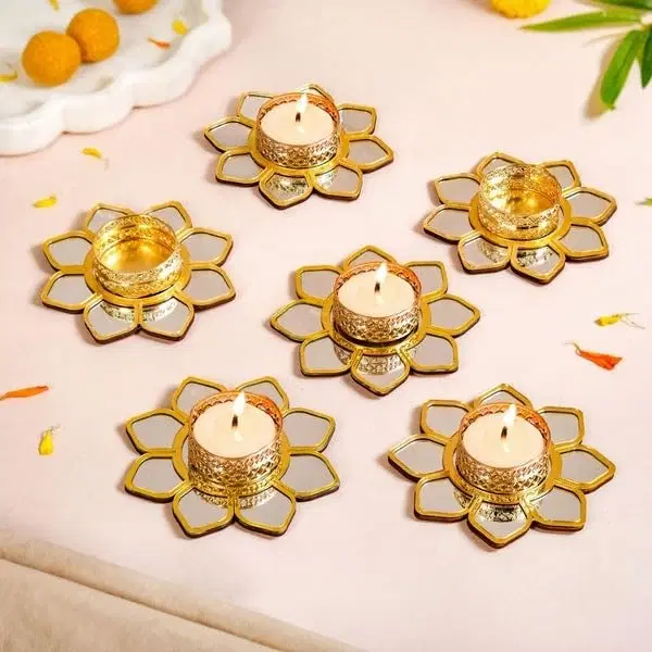 Six gold lotus tealight holders with mirrored petals arranged on a pastel surface, some holding lit candles