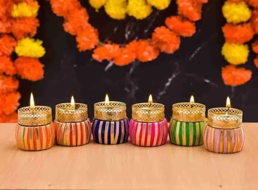 Six lit striped tealight holders with gold lattice rims lined up before orange and yellow marigold garlands
