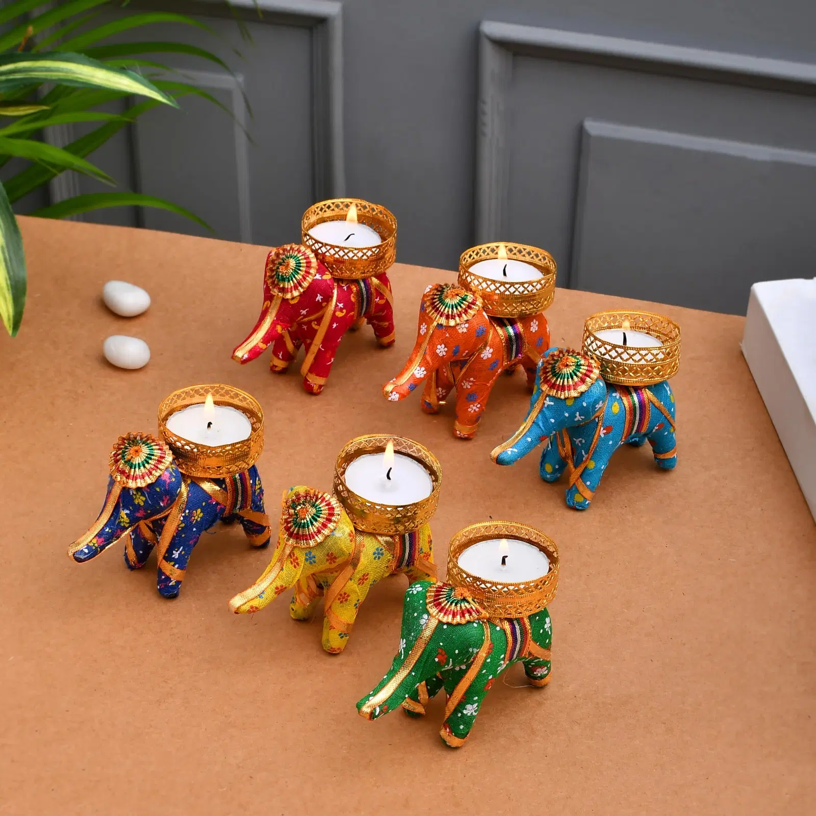 Set of 6 colorful elephant tea light holders with lit candles arranged on a tabletop