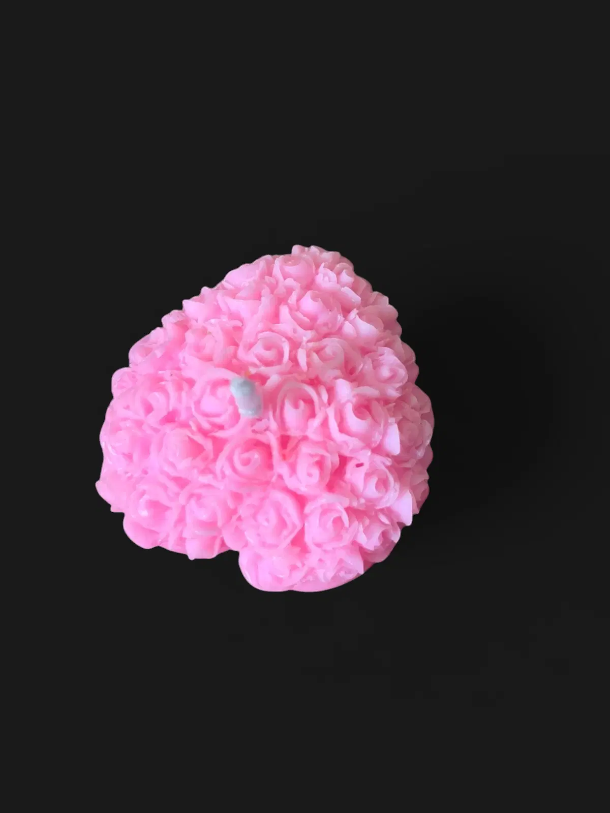 Pink rose-cluster decorative candle with visible wick on a maroon fabric background