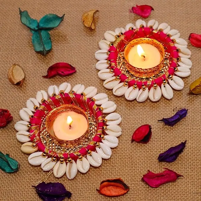 Two lit shell-decor diya holders on jute fabric with scattered dried petals