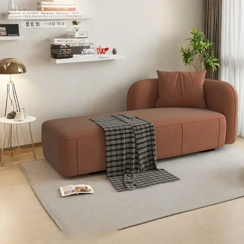 Brown upholstered chaise lounge sofa with rounded armrest, matching cushion and plaid throw in a styled room