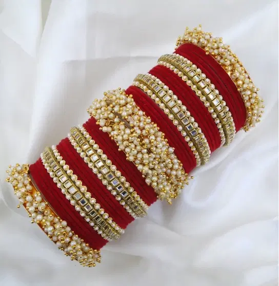 Red bridal bangle stack with kundan-style stone bands and pearl cluster edges on white draped fabric