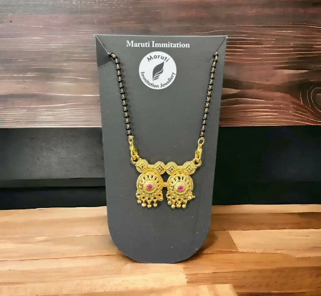 Gold-toned mangalsutra with black beads on branded black display card against a wooden backdrop