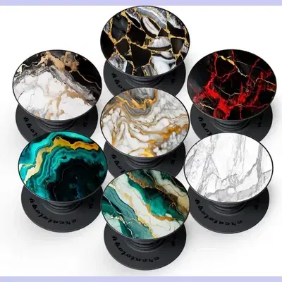Seven black collapsible phone grips with assorted marble and agate print tops on white background