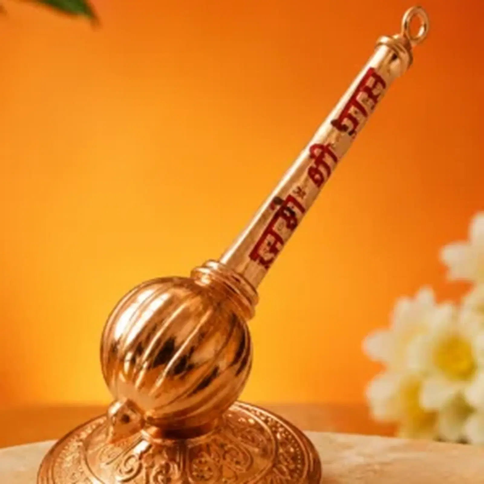 Close view of copper-toned pooja bell with Ram text on handle against warm orange backdrop