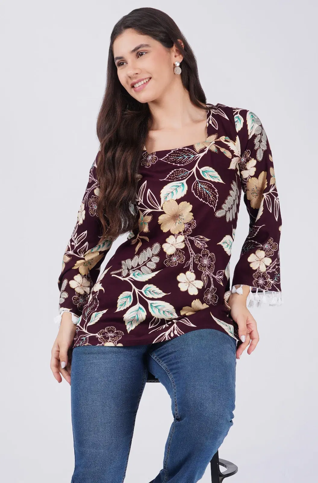 Front view of burgundy floral top with square neckline, full sleeves and tassel-trim cuffs worn with blue jeans