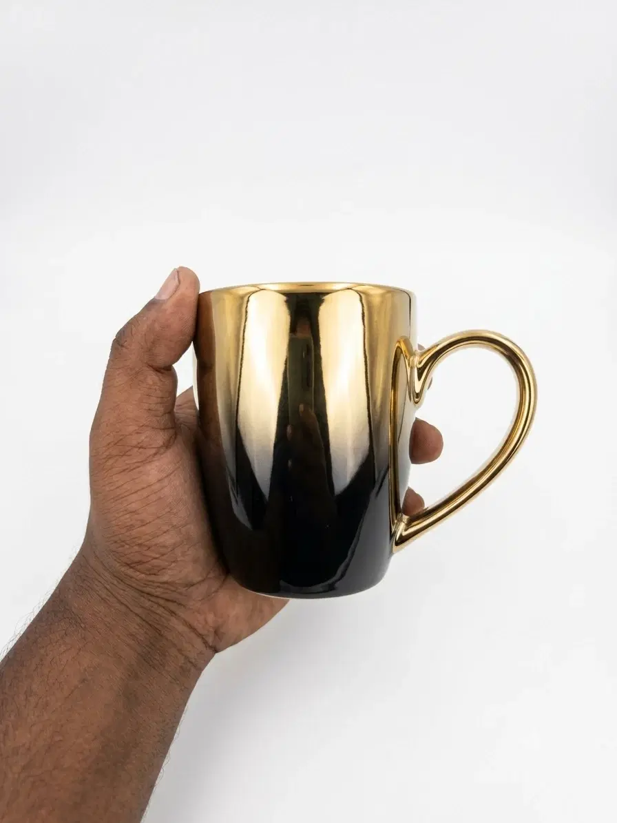 Hand-held view of glossy black to gold gradient ceramic mug with heart-shaped gold handle