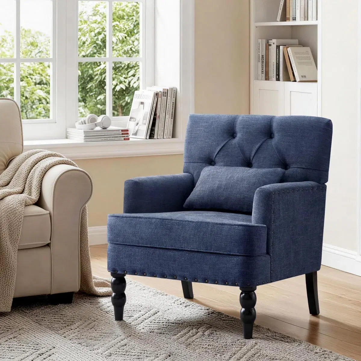 Blue upholstered accent chair with tufted back and pillow, styled beside a window in a living room