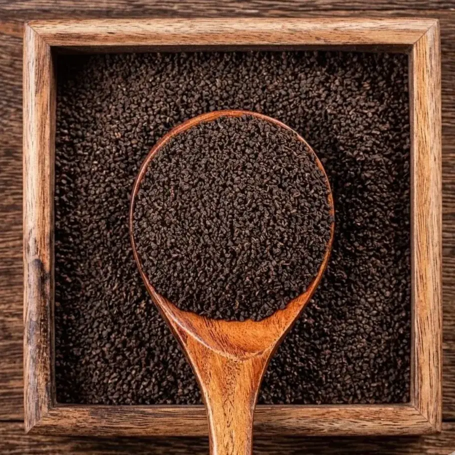 Loose Assam CTC tea granules in a wooden spoon over a wooden tray