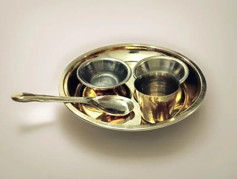 Top-down view of a shiny pure brass miniature bhog thali set featuring small bowls and a spoon.