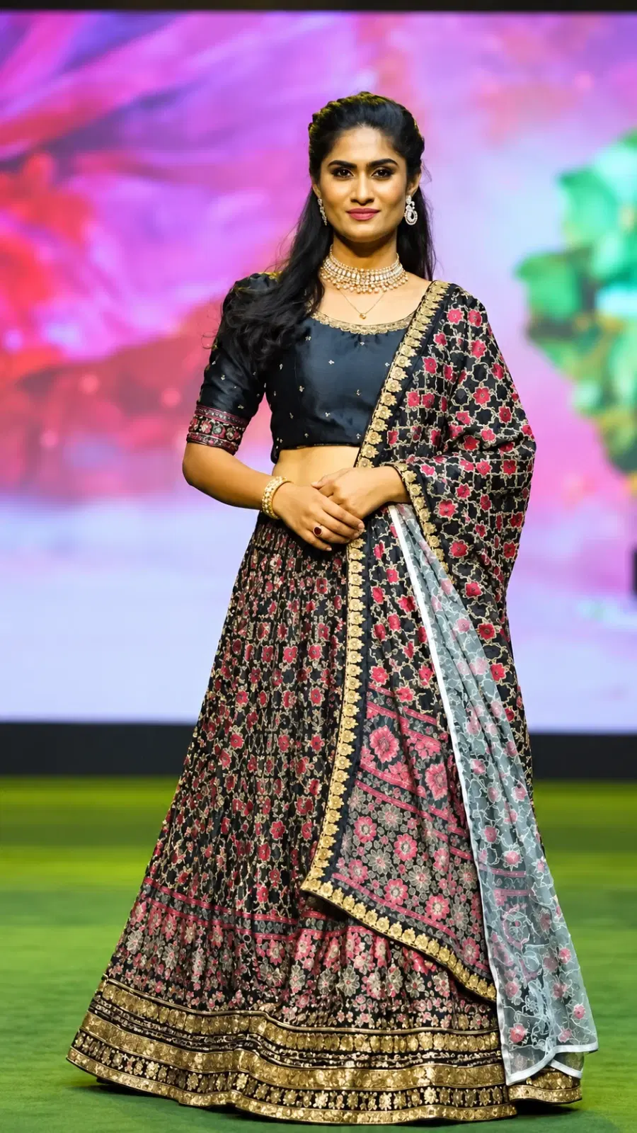 Front view of black floral lehenga set with gold border and matching dupatta worn on a runway