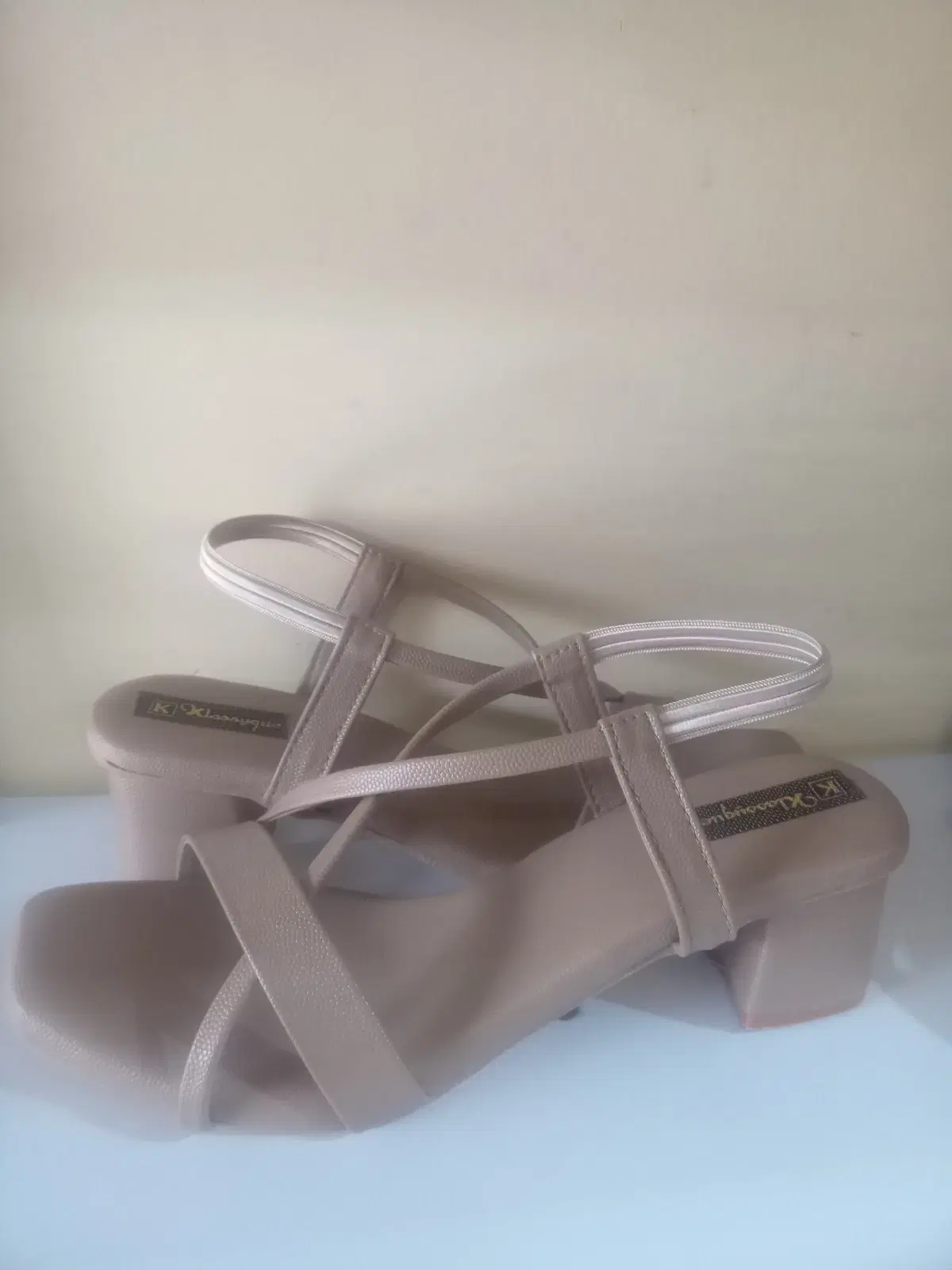Side view of beige slingback sandals with cross straps and mid block heels on a white surface