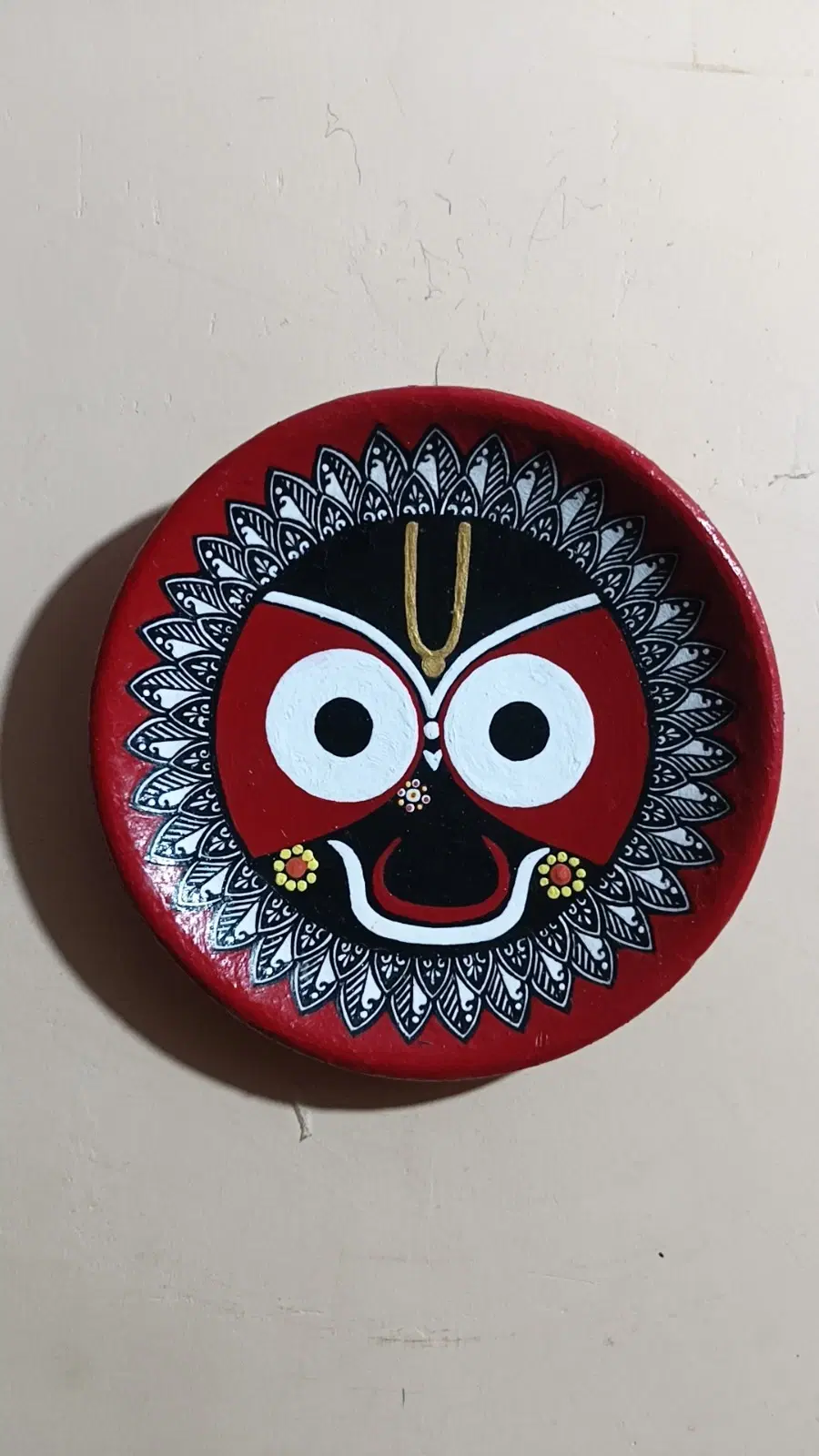 Front view of round red wall plate with hand-painted Jagannath face and black-white petal border