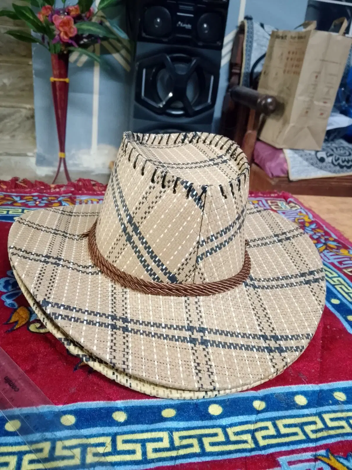 Natural woven cowboy hat with black check pattern and brown braided band on a colorful cloth