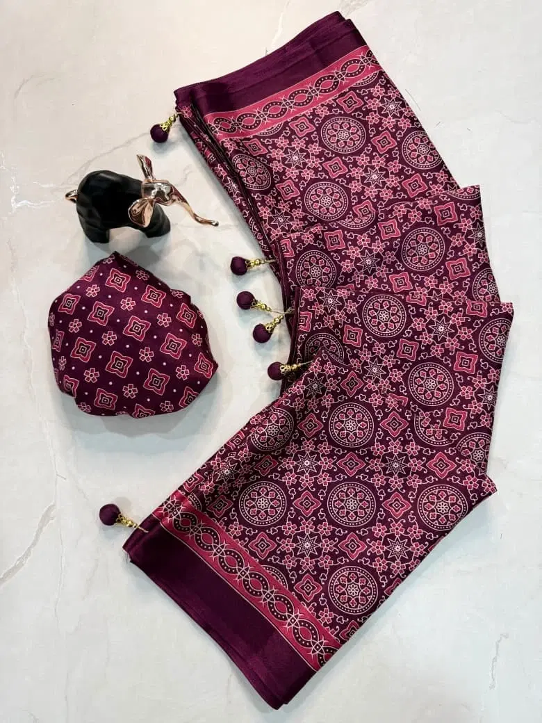 Folded maroon printed saree with tassel border and matching potli pouch on a light background